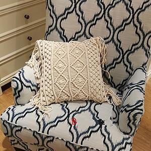 Hand-woven macrame cotton cushion cover on a rustic wooden bench with boho décor