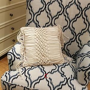 Hand-woven macrame cotton cushion cover on a rustic wooden bench with boho décor