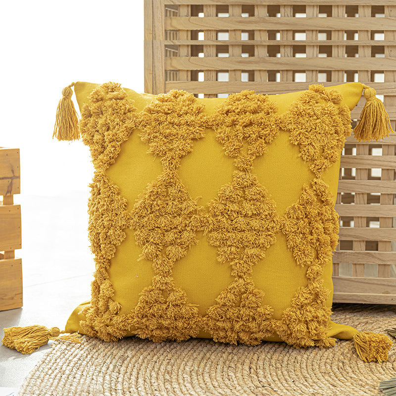 Tufted throw pillow with tassels placed on a cozy sofa in a boho-styled living room

