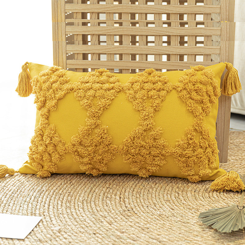 Tufted throw pillow with tassels placed on a cozy sofa in a boho-styled living room

