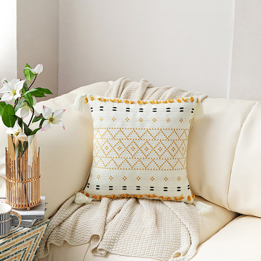 Hand-embroidered tufted pillowcase with fringe on a cozy sofa in a rustic living room



