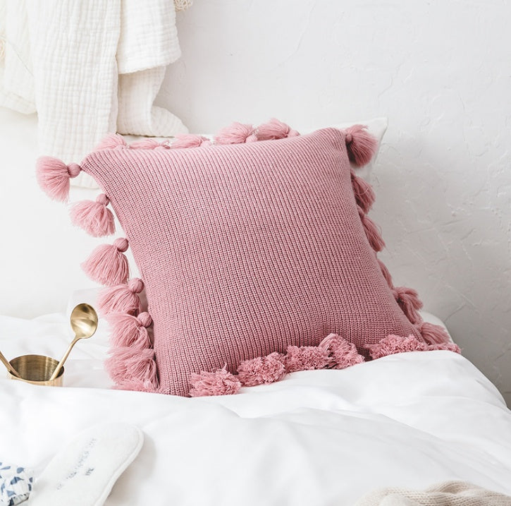 Bohemian knitted cushion cover with fringe on a sofa styled with cozy layered pillows

