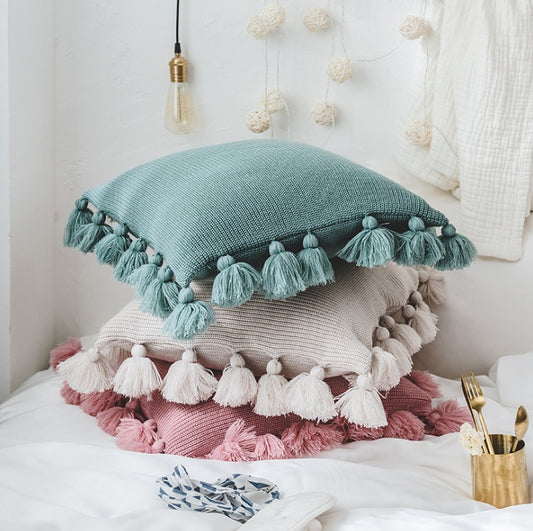Bohemian knitted cushion cover with fringe on a sofa styled with cozy layered pillows

