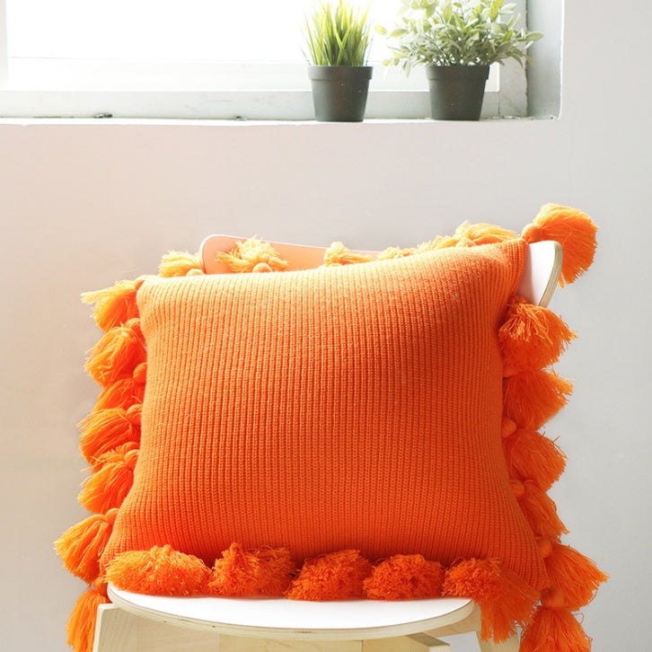 Bohemian knitted cushion cover with fringe on a sofa styled with cozy layered pillows

