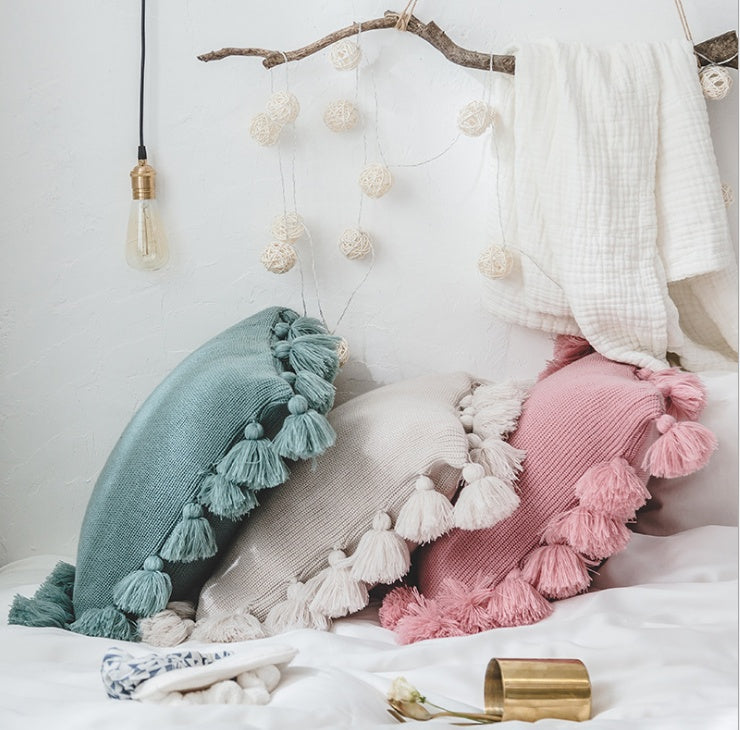 Bohemian knitted cushion cover with fringe on a sofa styled with cozy layered pillows


