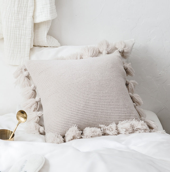 Bohemian knitted cushion cover with fringe on a sofa styled with cozy layered pillows

