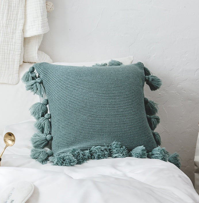 Bohemian knitted cushion cover with fringe on a sofa styled with cozy layered pillows

