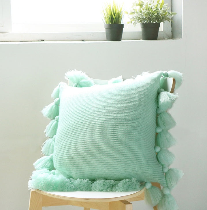 Bohemian knitted cushion cover with fringe on a sofa styled with cozy layered pillows

