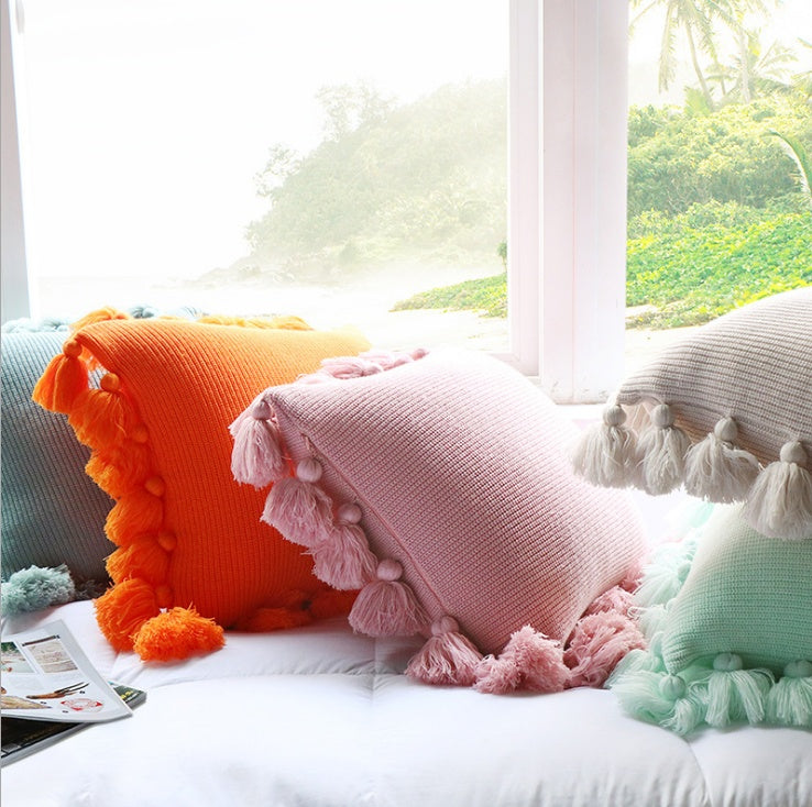 Bohemian knitted cushion cover with fringe on a sofa styled with cozy layered pillows

