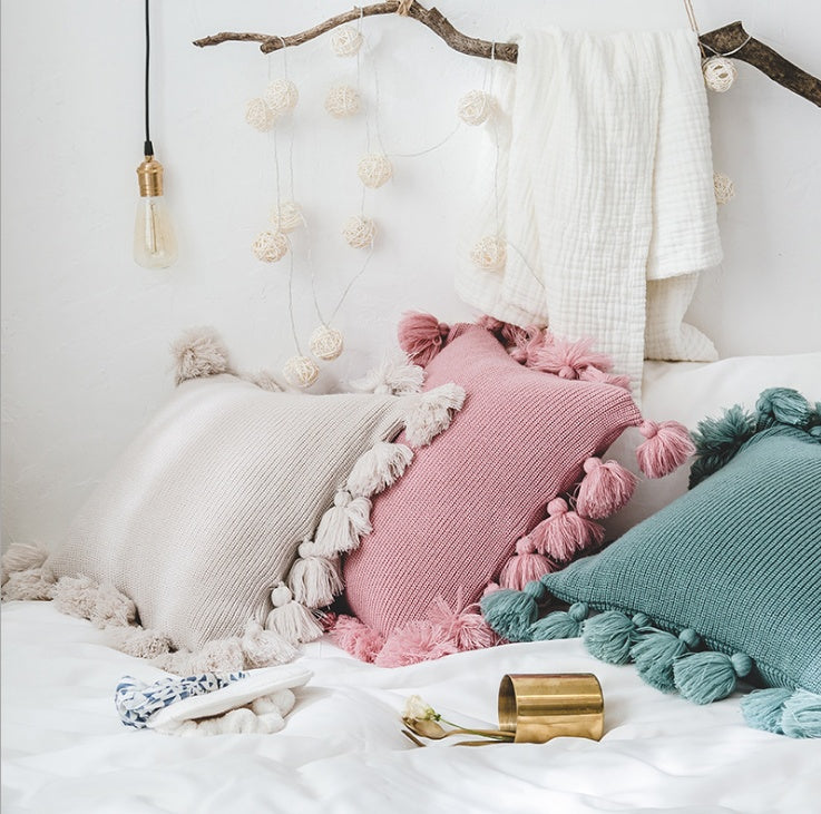 Bohemian knitted cushion cover with fringe on a sofa styled with cozy layered pillows

