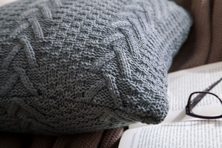 Thick wool knitted pillowcase with chunky knit pattern on a cozy sofa

